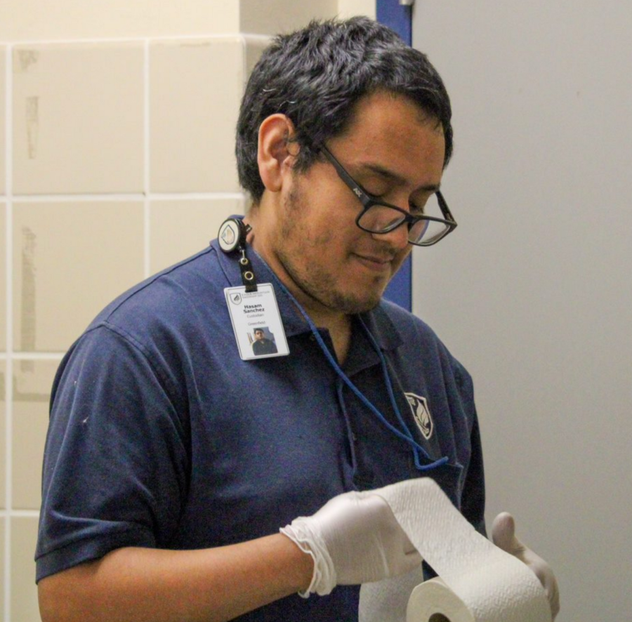 Custodian Hasam Sanchez replaces toilet paper in a bathroom after school.